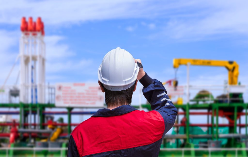 Rear view of engineer wearing white safety helmet before working on oil tanker ship at shipyard